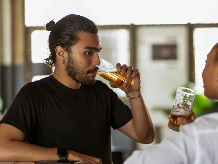 the man is drinking from the glass and looking at the woman