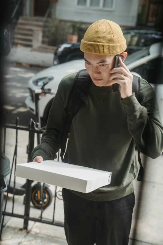 man with yellow hat walking down the street talking on cell phone