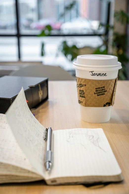 an open notebook next to a coffee cup with a pen