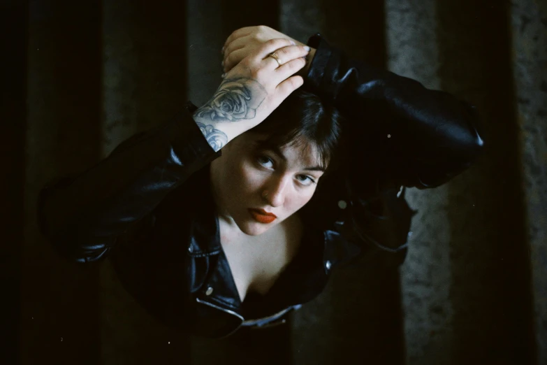 a girl in black jacket and tattoos with her arm over her head