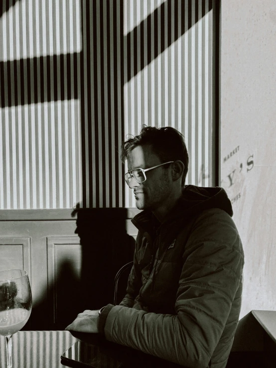 a man wearing glasses is sitting next to a glass with a drink