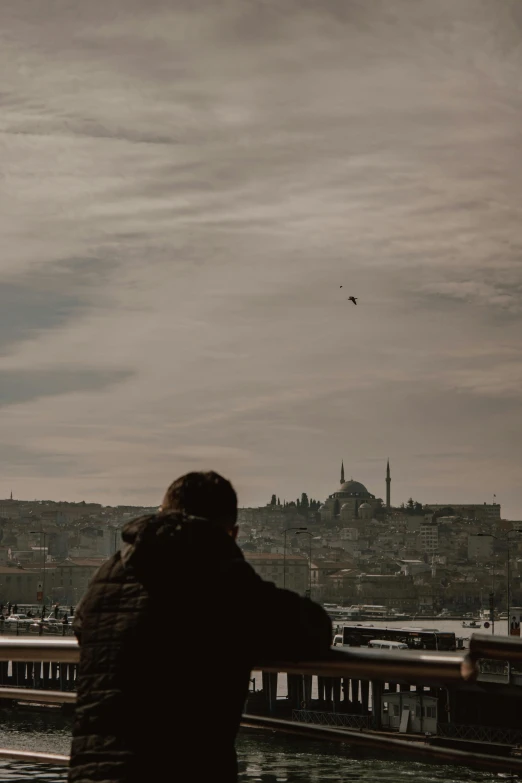 a man standing outside looking at an airplane that is flying over a city