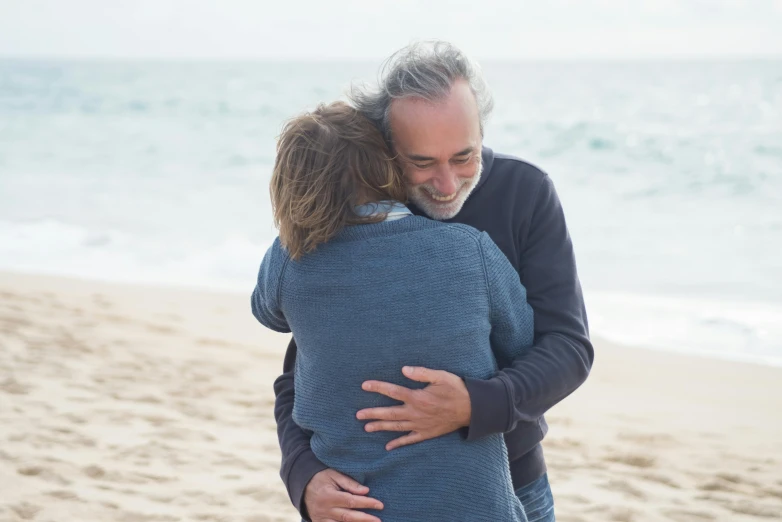 an older man hugs a younger woman on the beach