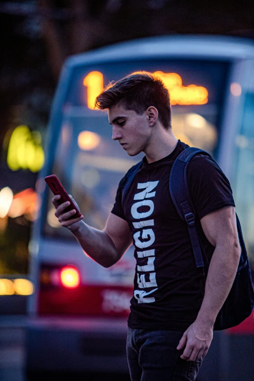 a young man using his phone in front of the city bus