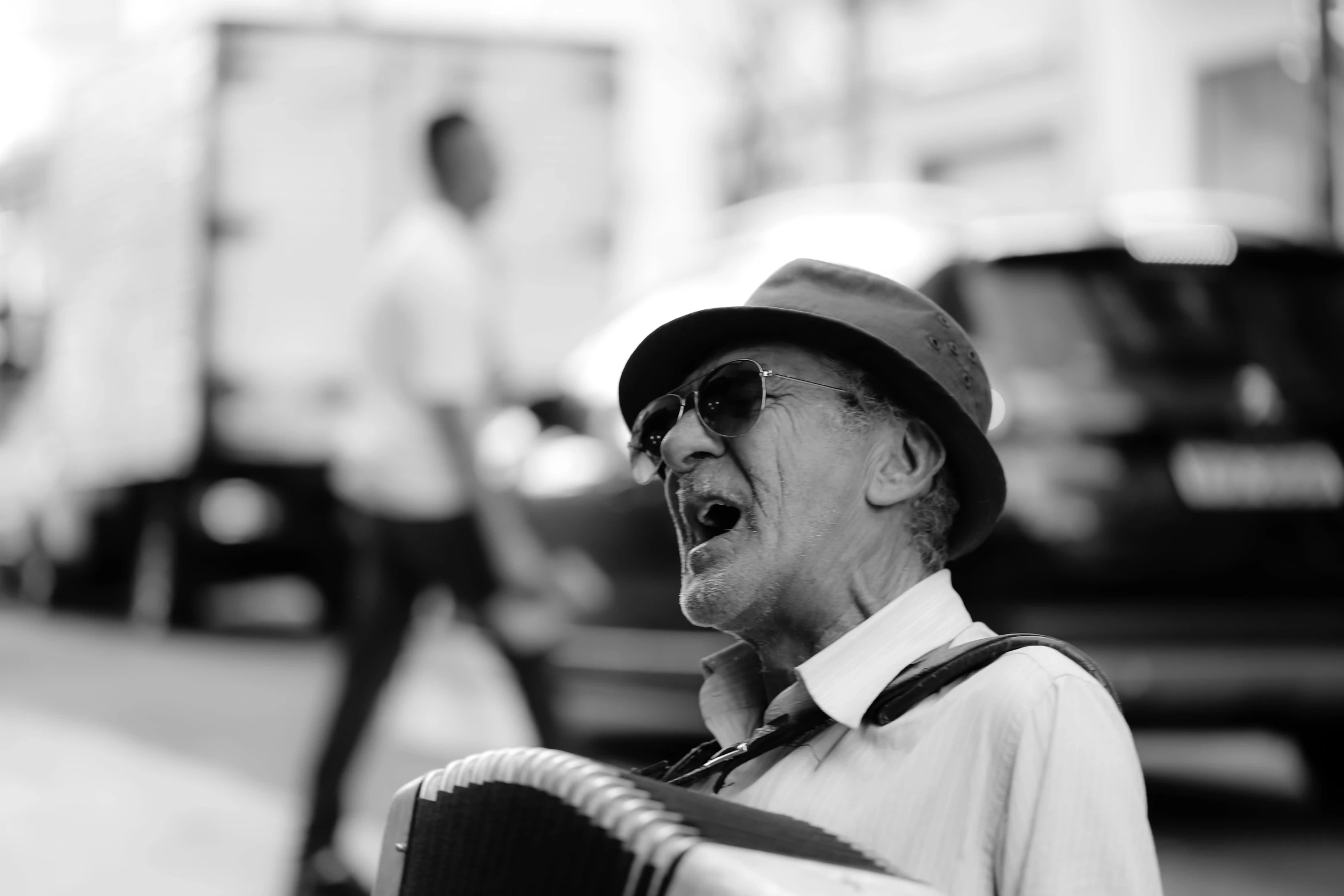 a man in a hat, tie, and glasses singing into an accordion