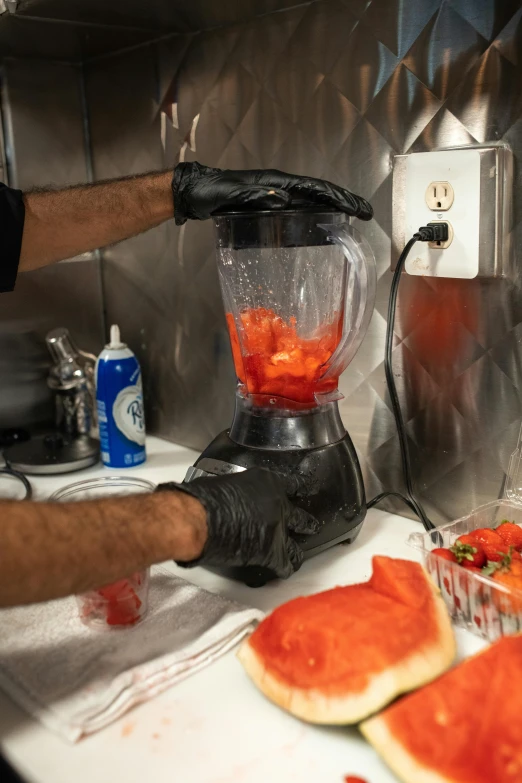 two watermelon slices in front of the blender and a person peeling it