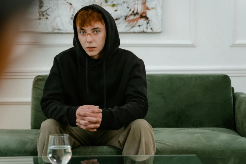 a man wearing a hoodie sits on a green couch