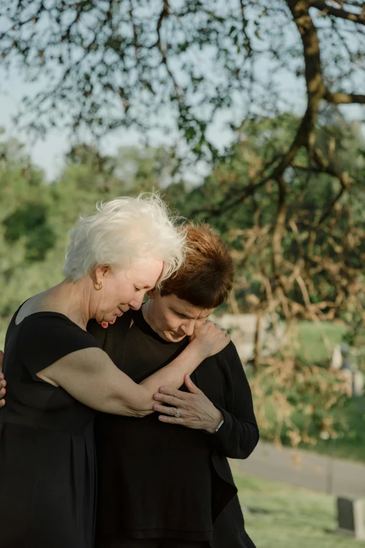 an older woman hugging another older woman in front of trees
