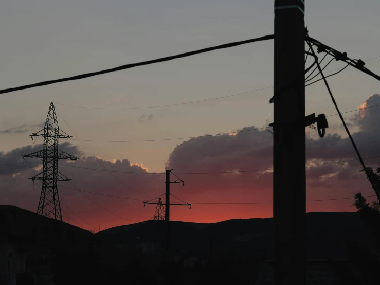 an electric pole sitting below power lines in the sunset