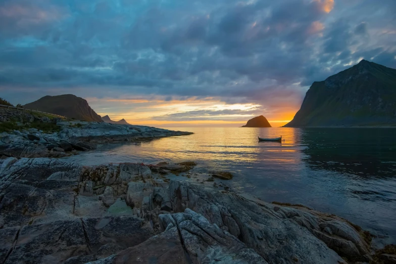 a sunset on a rocky coast with a boat in the distance