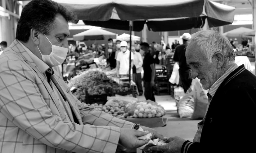 two men wearing masks on the street outside an outdoor farmers market