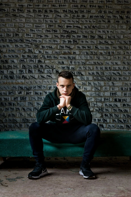 man kneeling on a bench in front of a wall with writing