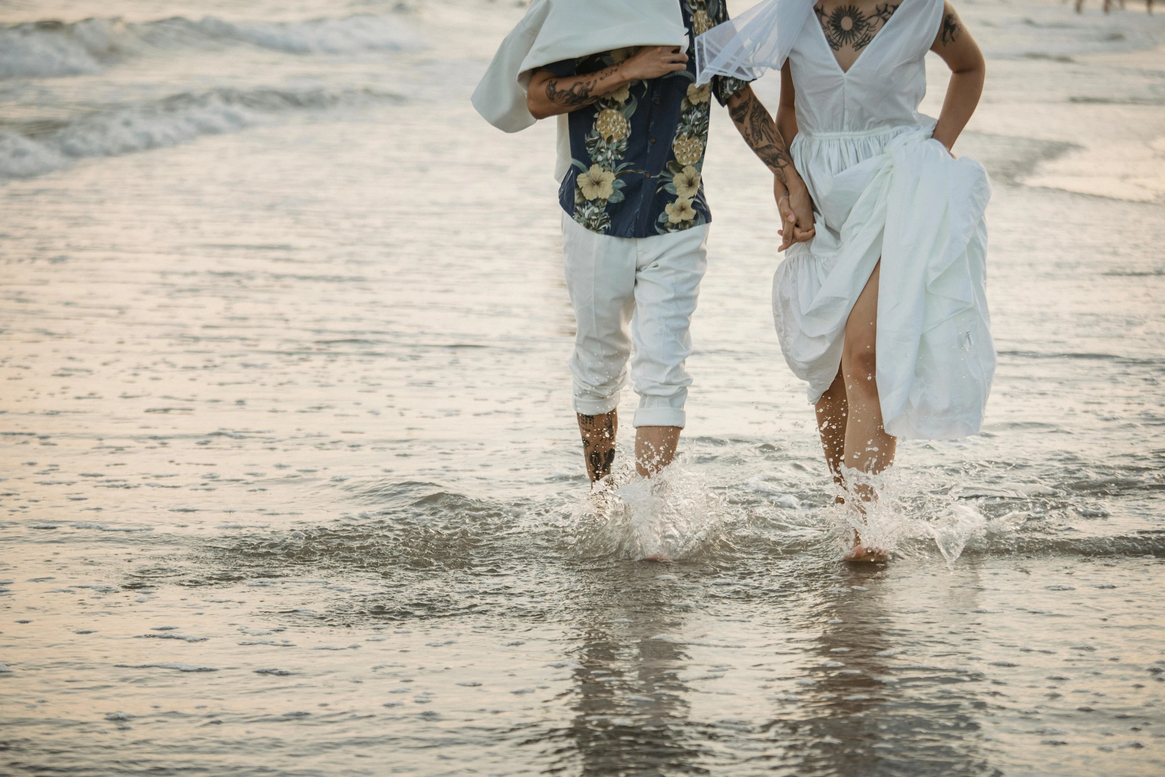 a man and woman walk together through the water on a beach