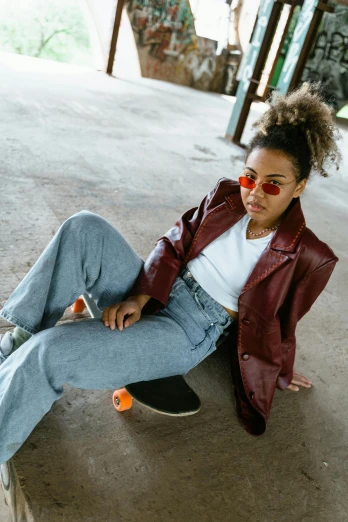 a woman sitting on the ground wearing sunglasses and holding a skateboard