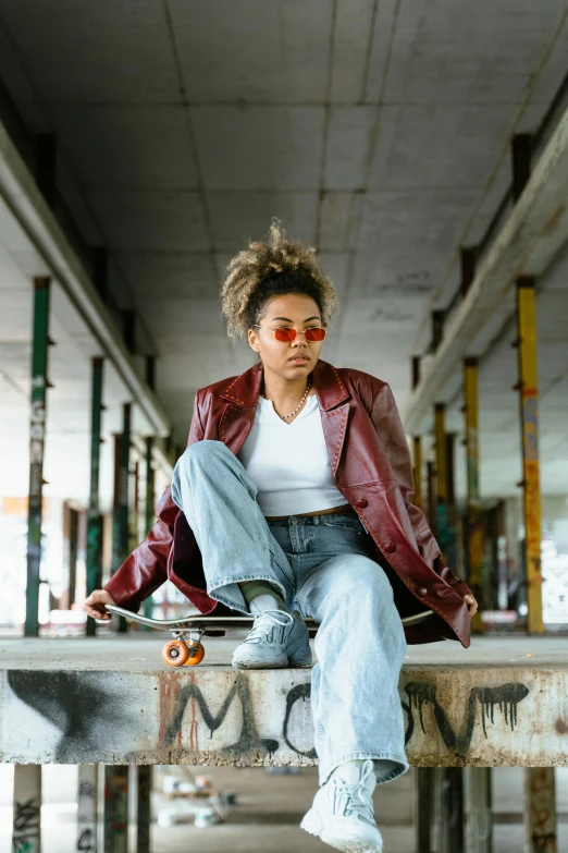 woman with red jacket and jeans sitting on a wall with skateboard