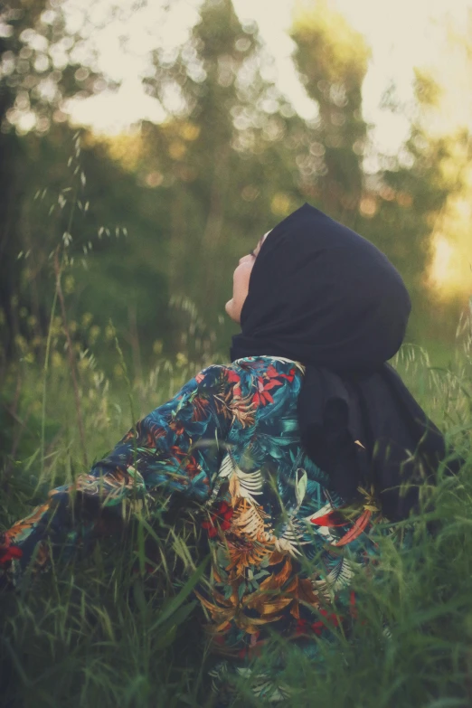 a person with a head scarf on is sitting in the grass