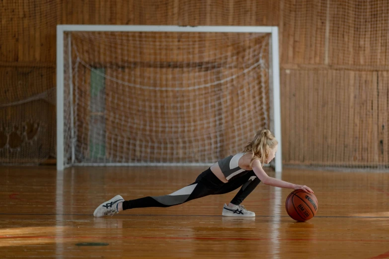 a girl stretches to touch her knees as she stands in front of a ball
