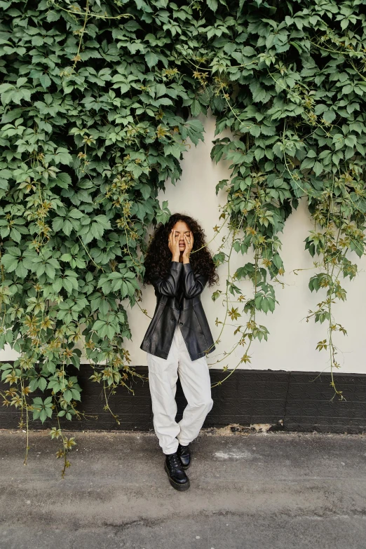 the young person is posing for the camera near a wall covered in ivy