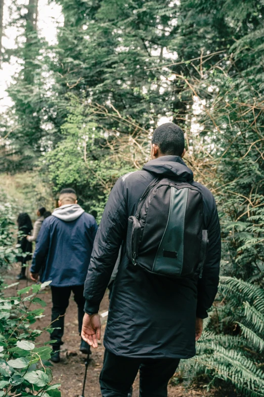 a man and woman walk in the woods wearing backpacks