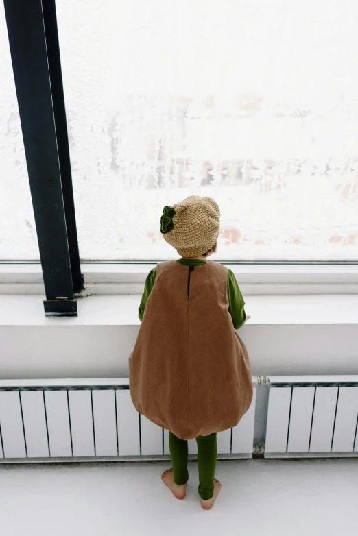 a child in brown jacket standing at window next to a building