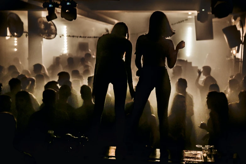 two women in dimly lit hall with several people