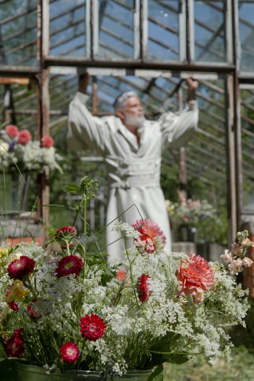 a man in white standing behind plants outside