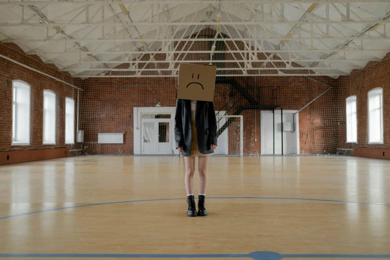 a man is standing in a basketball court with a cardboard box on his head