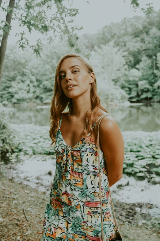 a girl in a colorful dress in front of trees near the water