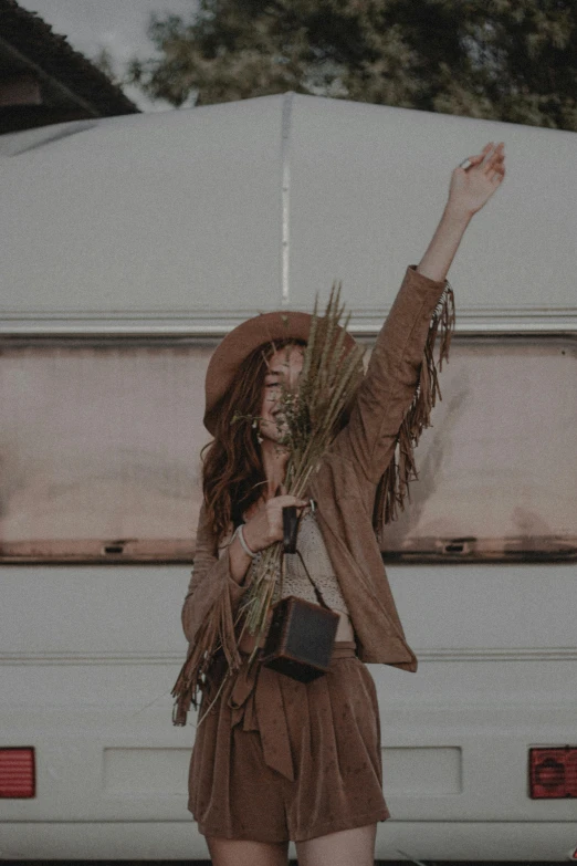 a woman wearing a brown dress and holding up an arm full of leaves