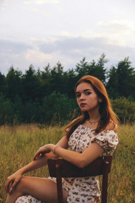 a beautiful young woman sitting on top of a wooden chair in a field