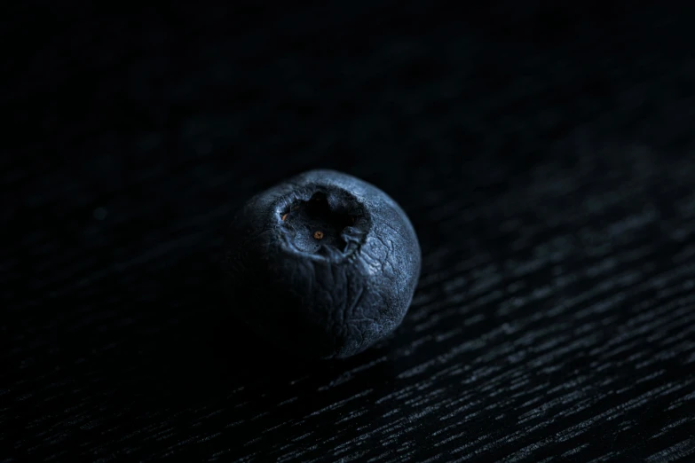 a whole black blueberry on a dark surface