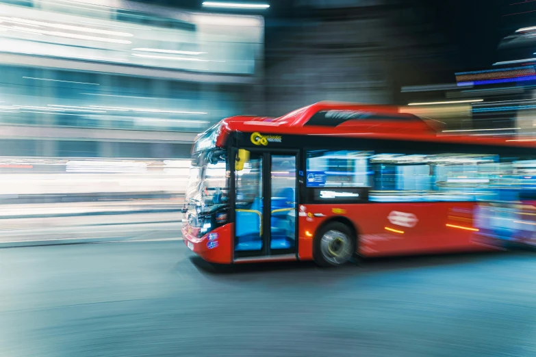 the red bus is driving by in front of buildings