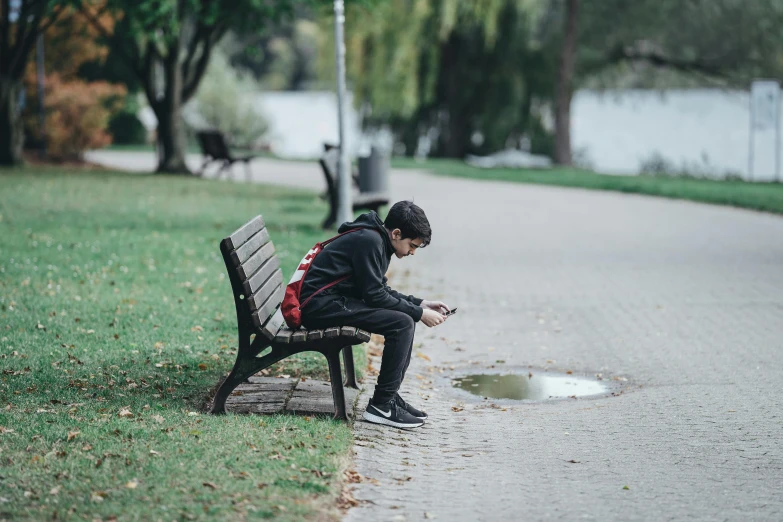 a man looking at his phone sitting on a bench in a park