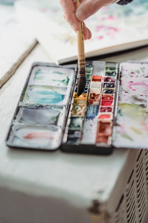 a close up of a person holding a brush in a paint palette near many other paint cans