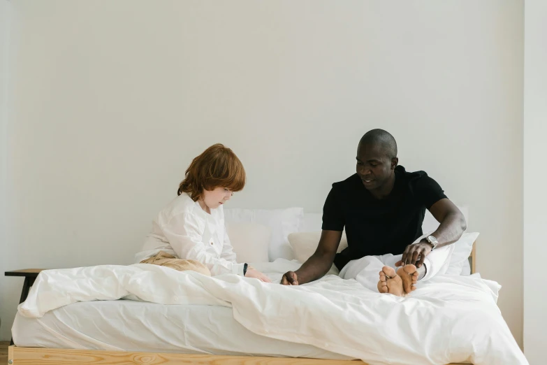 a father sits in bed with his daughter, who is sitting on the edge