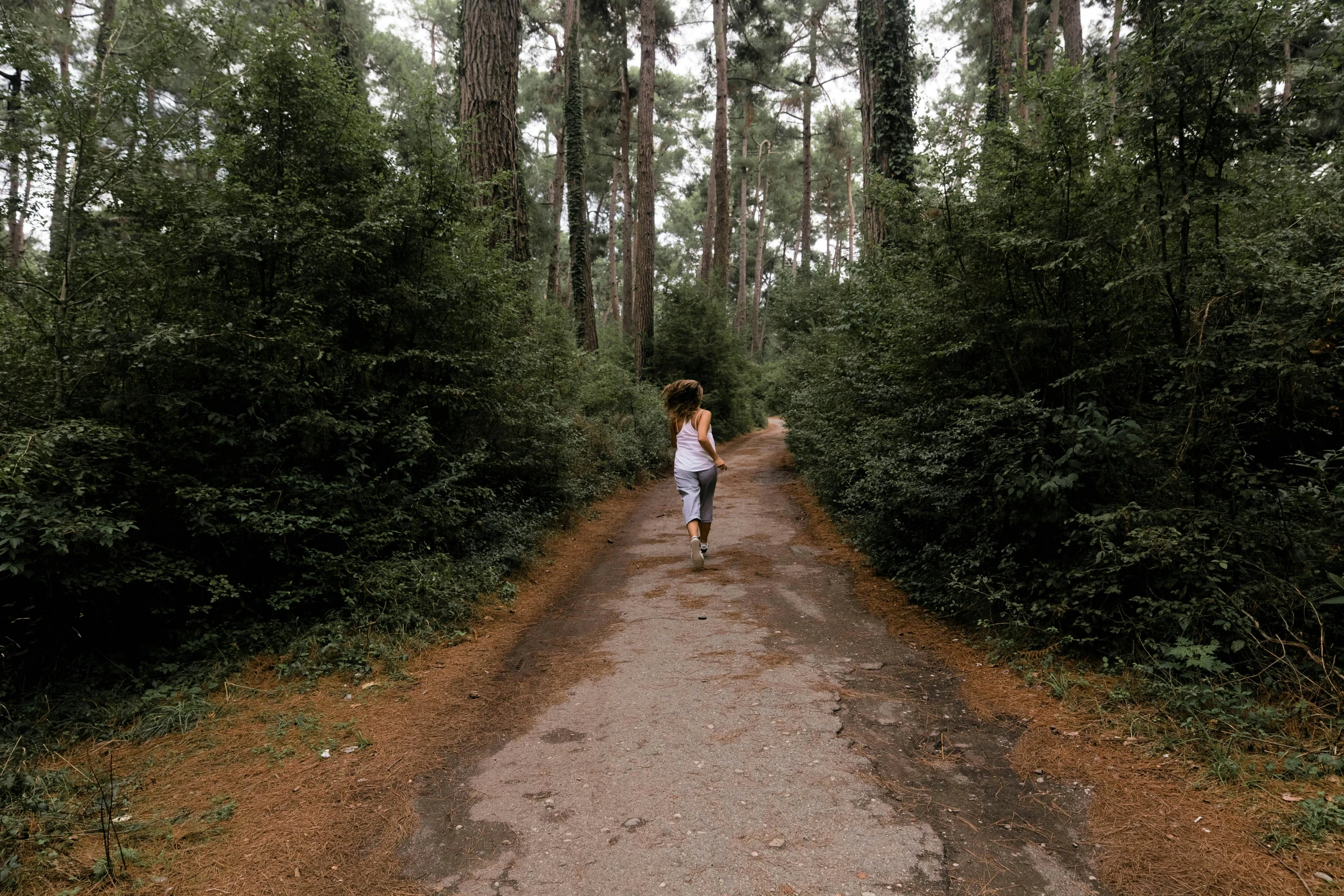 woman in white shirt walking down dirt road in woods