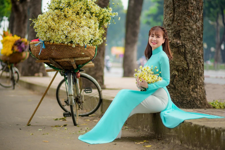 a woman sitting on the curb in front of a tree and bike with yellow flowers