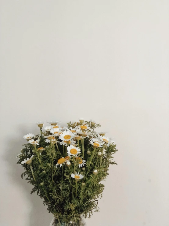 small vase with flowers on the table in front of a white wall