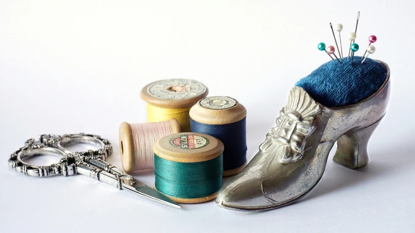 a silver shoe and spool of thread with some scissors and keychains