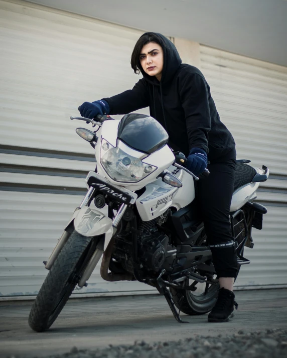 a woman poses on a motorcycle in front of a garage