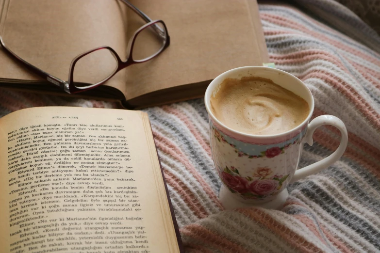 coffee cup and book on a bed next to eyeglasses