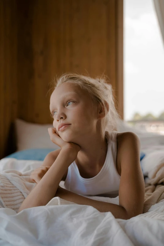 an adorable girl laying in bed with a white tank top