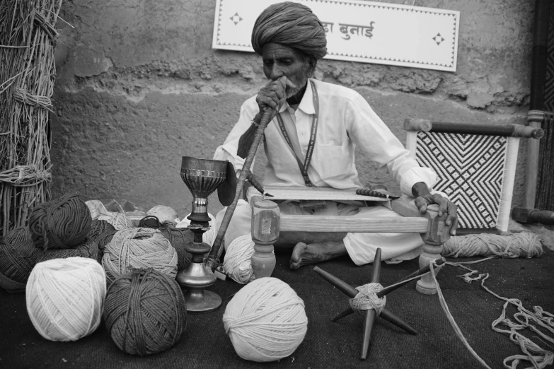 a man sitting on top of a bench in front of crocheted items