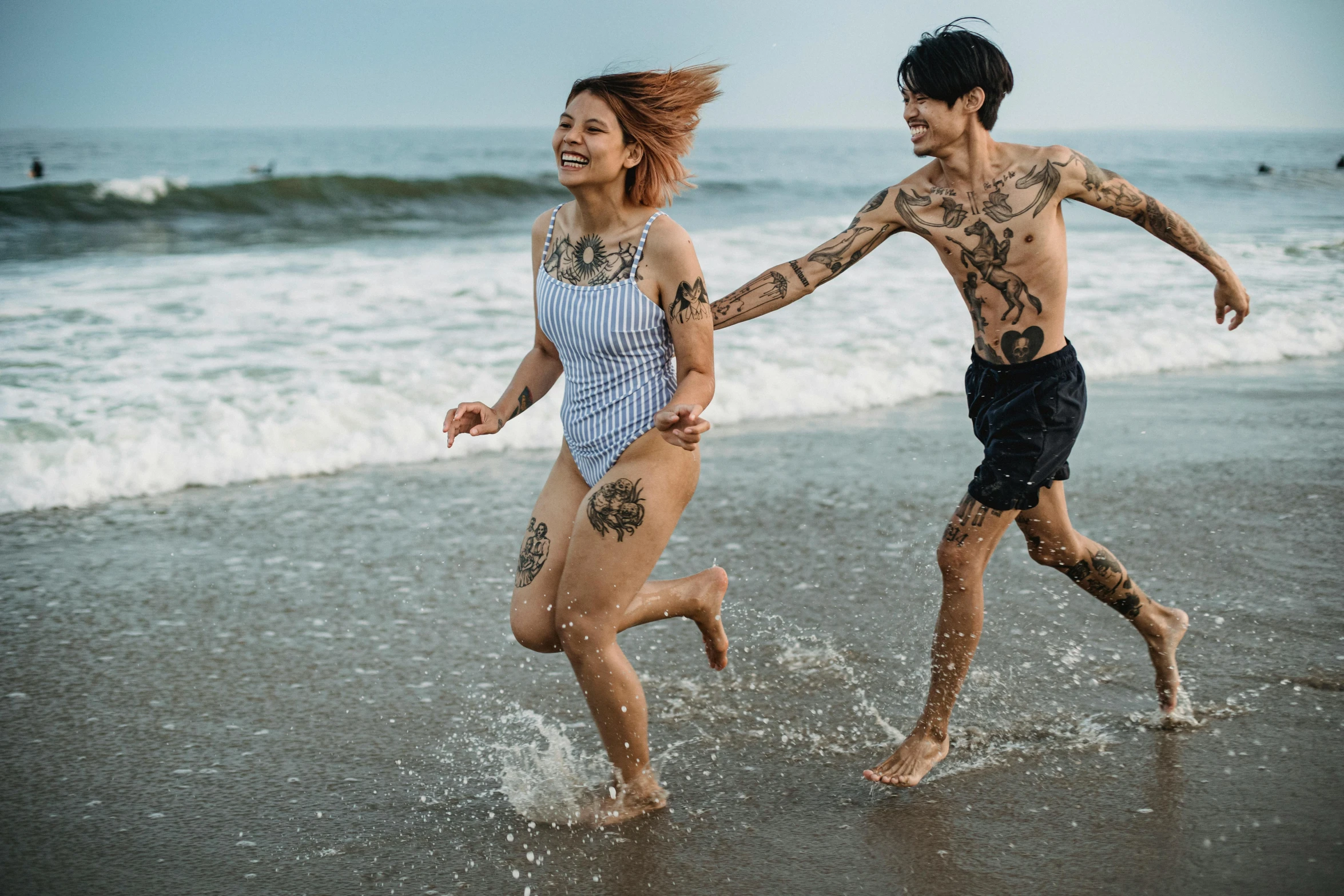 man and woman running into the ocean on a beach