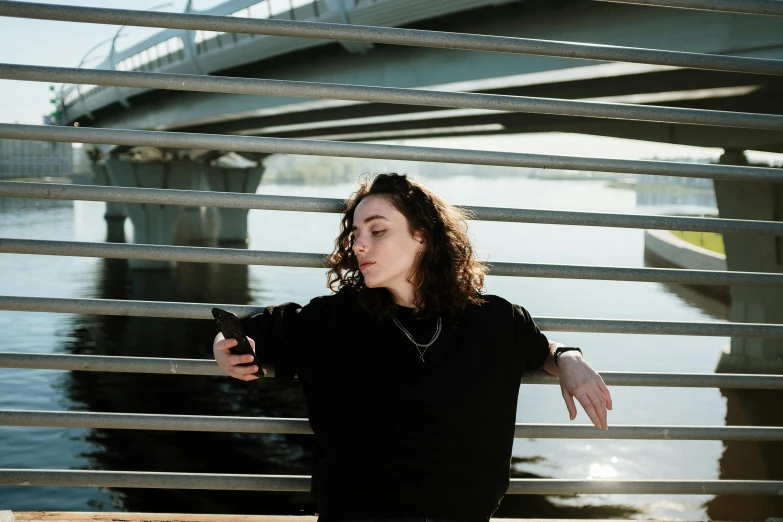 a woman holding a camera, in front of a bridge