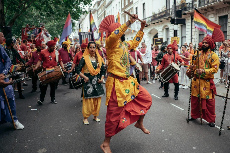 people with orange and yellow clothing are playing drums in a parade