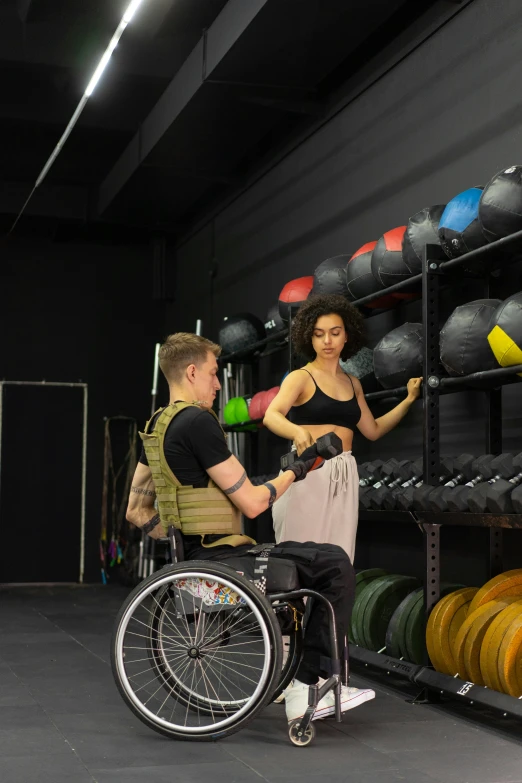 a man sitting in a wheelchair looking at a woman who has on a black tank top