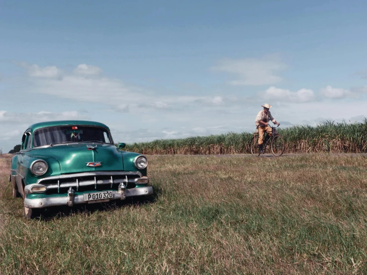 an old car parked in the middle of a field near a corn field