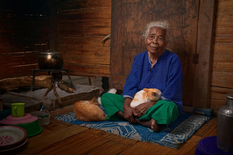 a woman sitting in front of a wooden wall holding a small dog