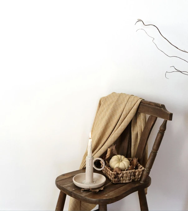 a basket with a white candle sitting on a chair in front of a wall